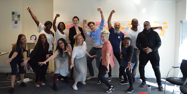 A group of people of different ages, genders and ethnicities looking happy with their arms up