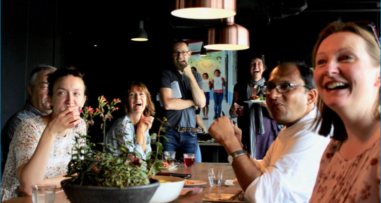 A group of people of different ages, genders and ethnicities sit at a table, looking up and smiling