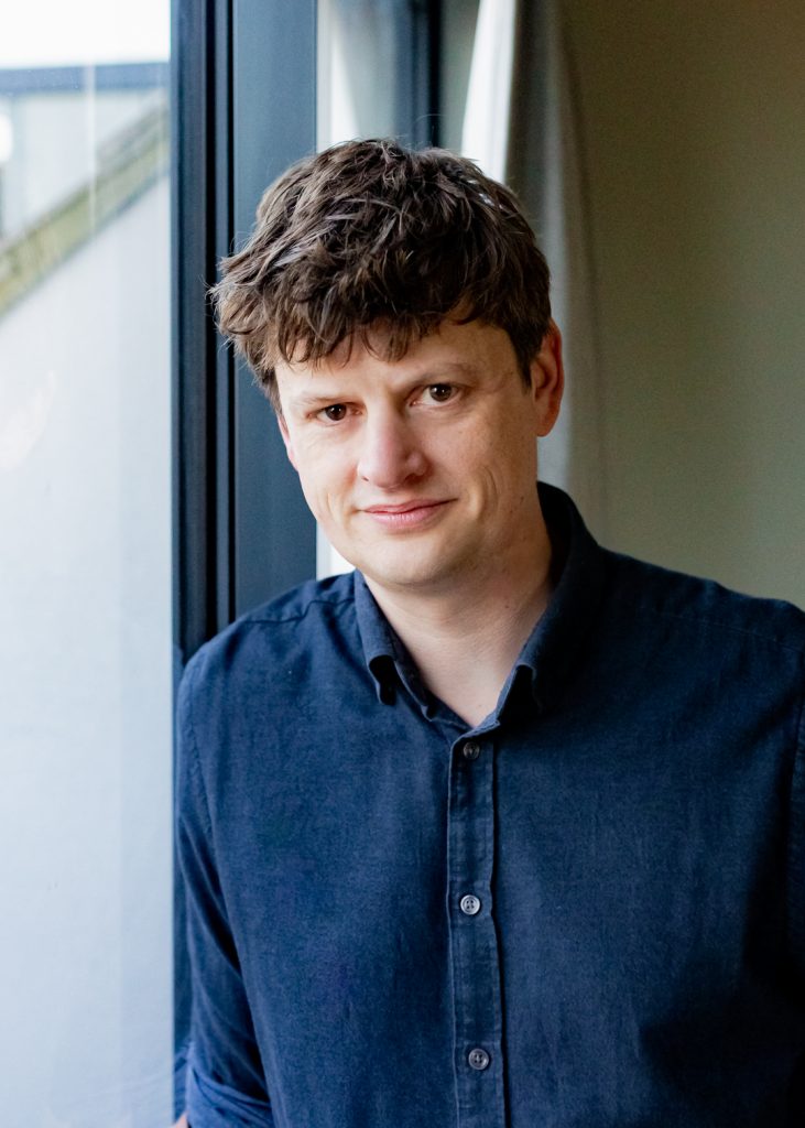 Simple Politics founder Tatton Spiller's headshot where he leans against a window facing the camera