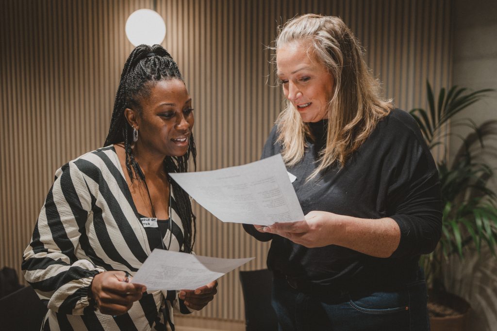 Two people talk to each other while reading from pieces of paper